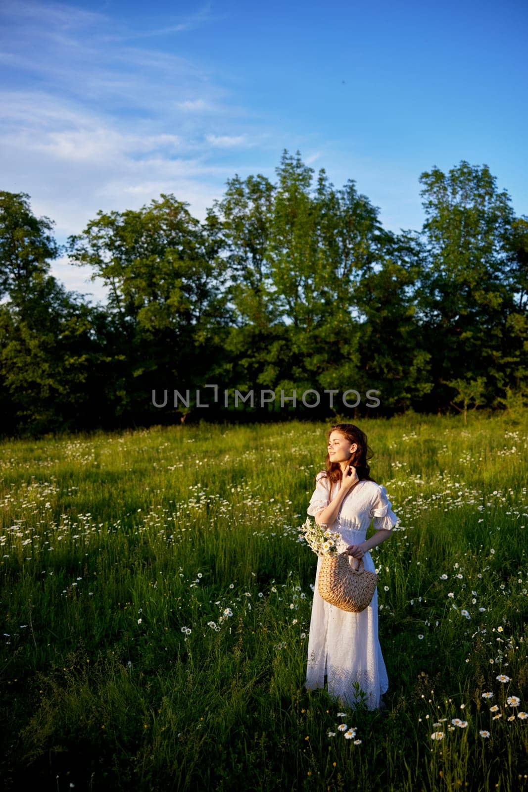 a beautiful woman stands in a flowering field on a sunny day in a light summer dress and with a wicker basket full of flowers by Vichizh