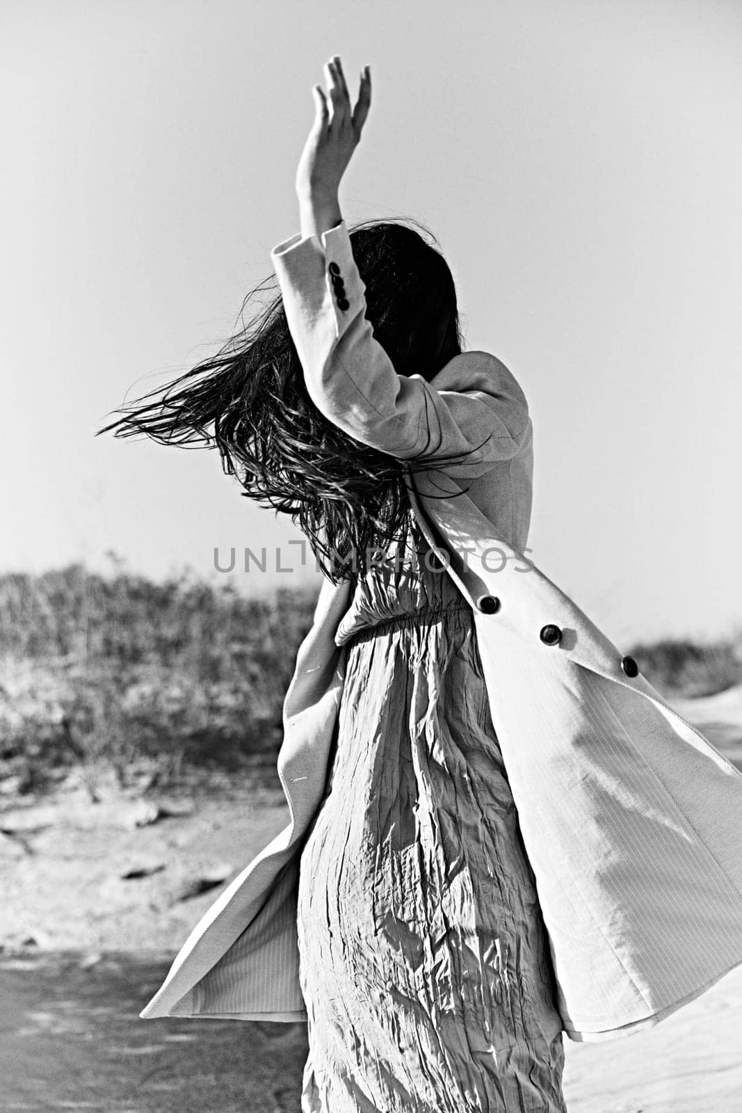 monochrome photo of a woman in a jacket against a clear sky on the coast posing with her hand raised up. High quality photo