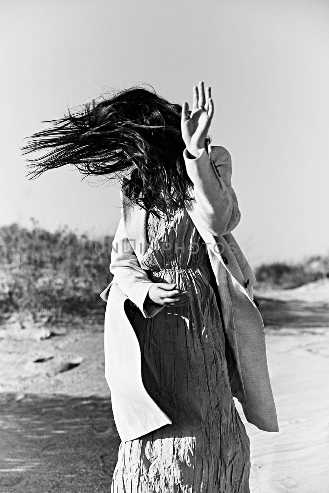 monochrome photograph of a twirling woman on the coast in a light-colored jacket with her face covered by her hair. High quality photo