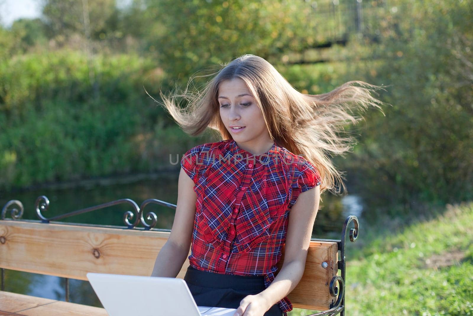 Girl on bench with laptop in autumn park- wind on hair
