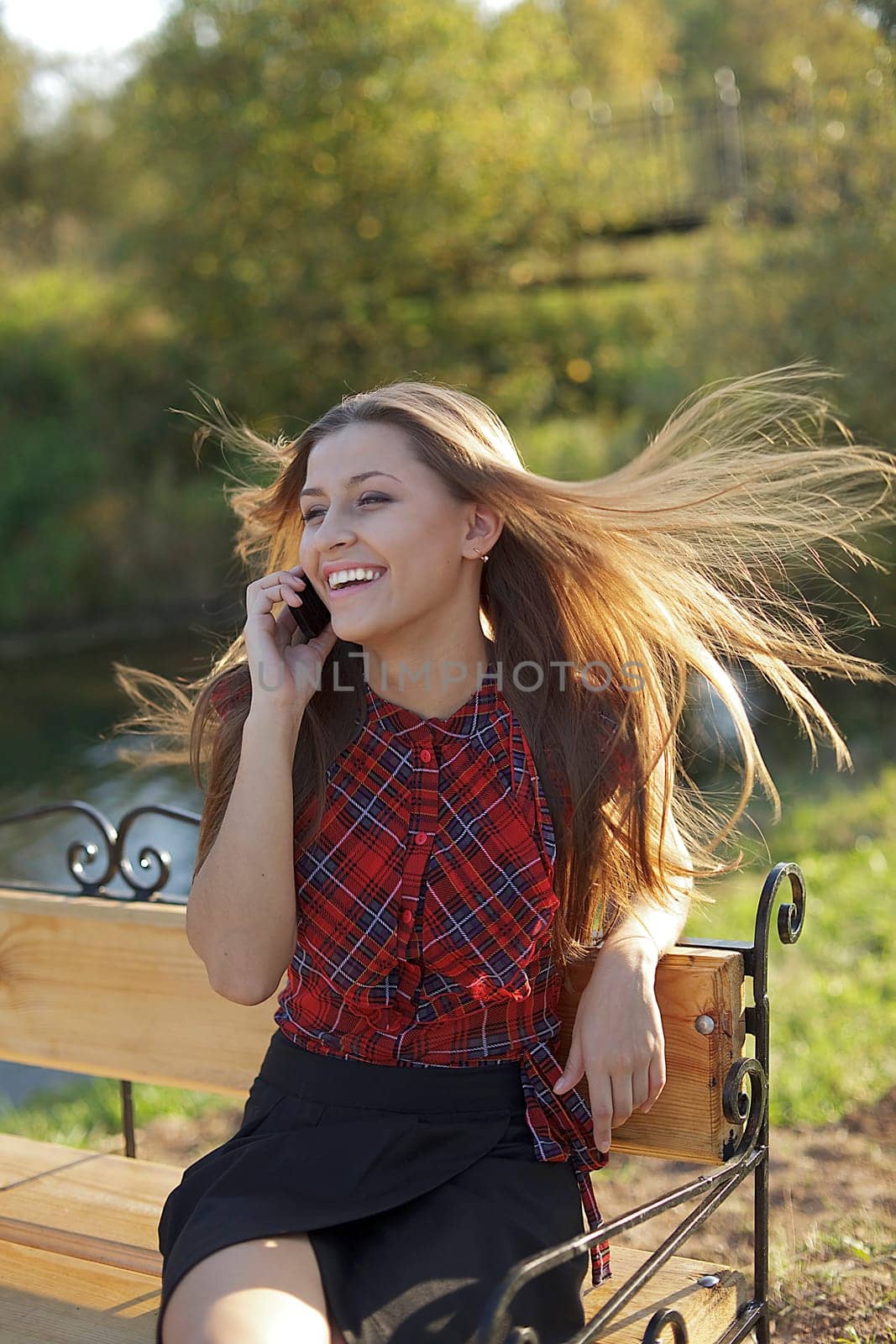 Woman on bench call phone in autumn park- wind on hair