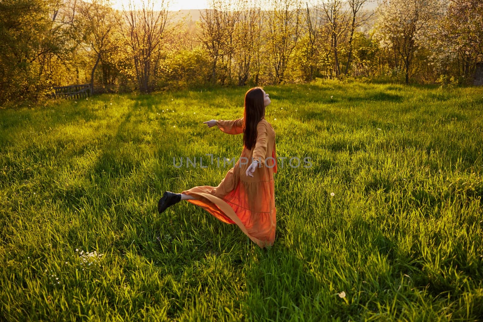 a joyful woman runs through a green field with her hands behind her back, enjoying a warm summer day and nature during the sunset. Horizontal photography in nature. High quality photo