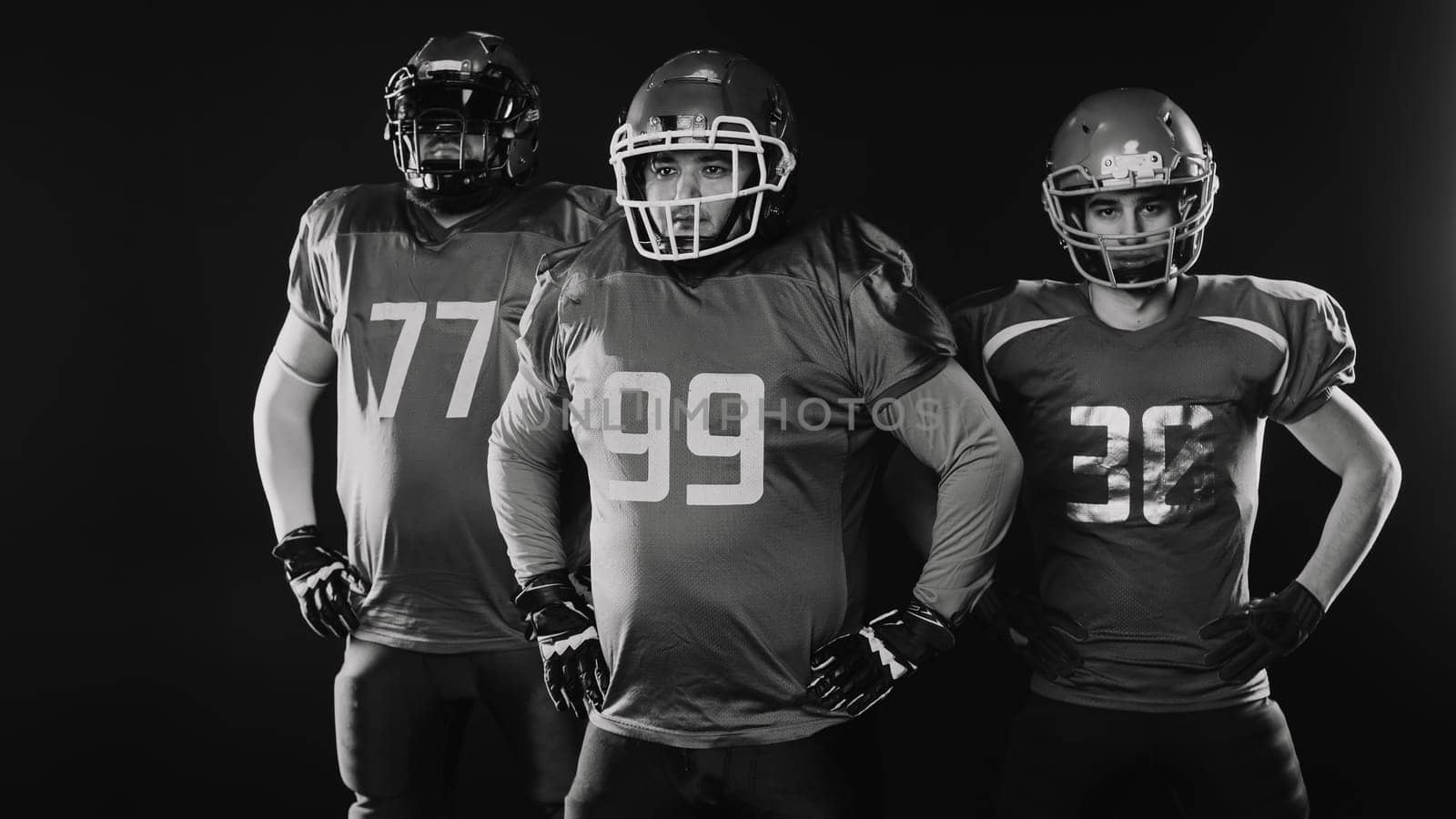 Portrait of three men in uniforms for American football on a black background. Monochrome