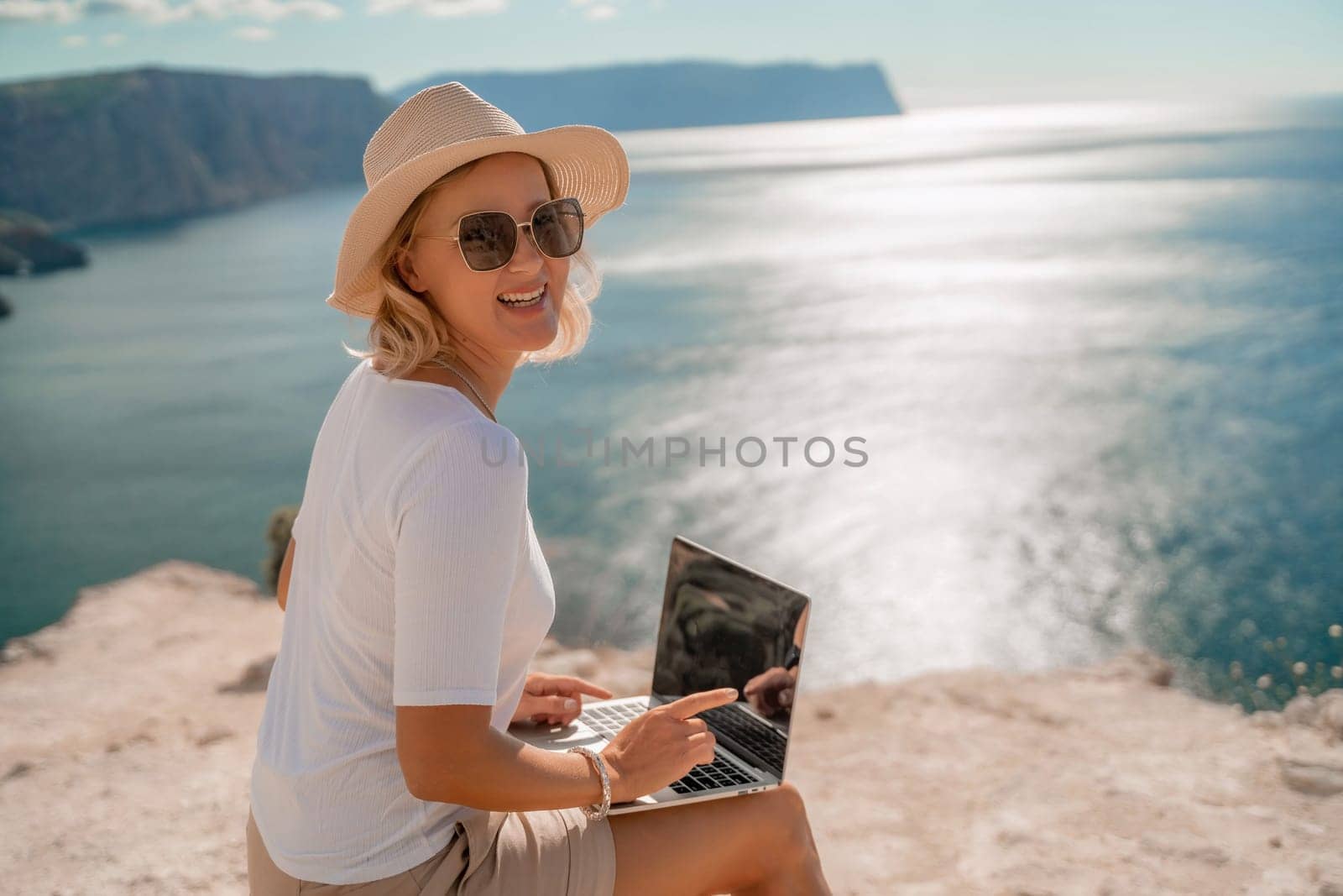 Freelance women sea working on the computer. Good looking middle aged woman typing on a laptop keyboard outdoors with a beautiful sea view. The concept of remote work. by Matiunina