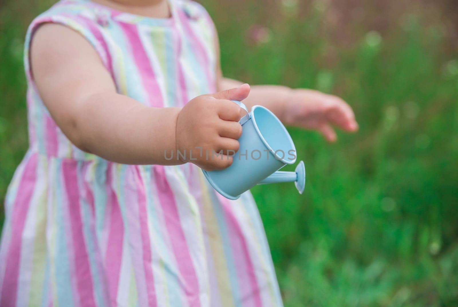blue watering can for flowers close-up in the hands of a baby.
