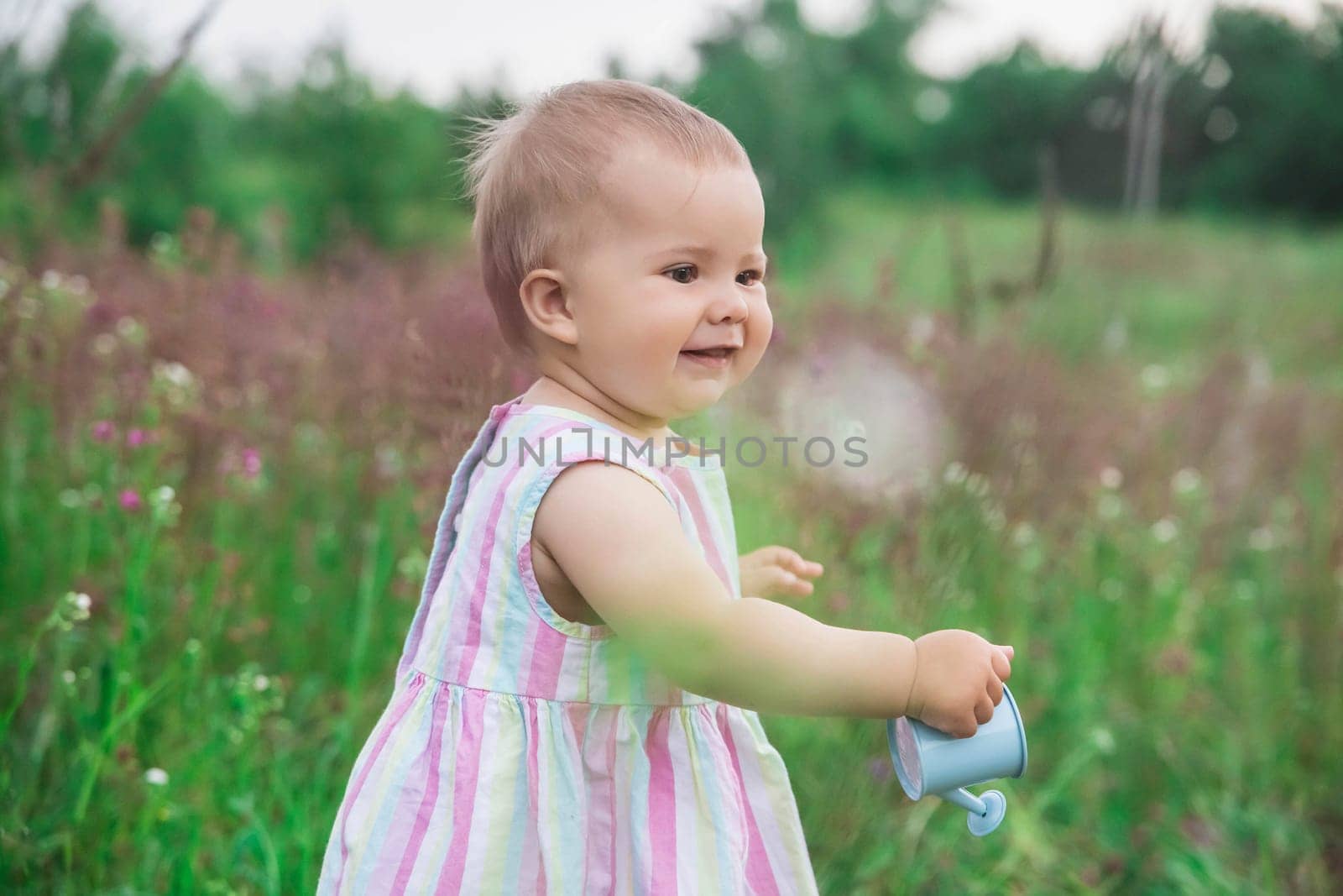 beautiful baby in a striped dress watering flowers in the garden.