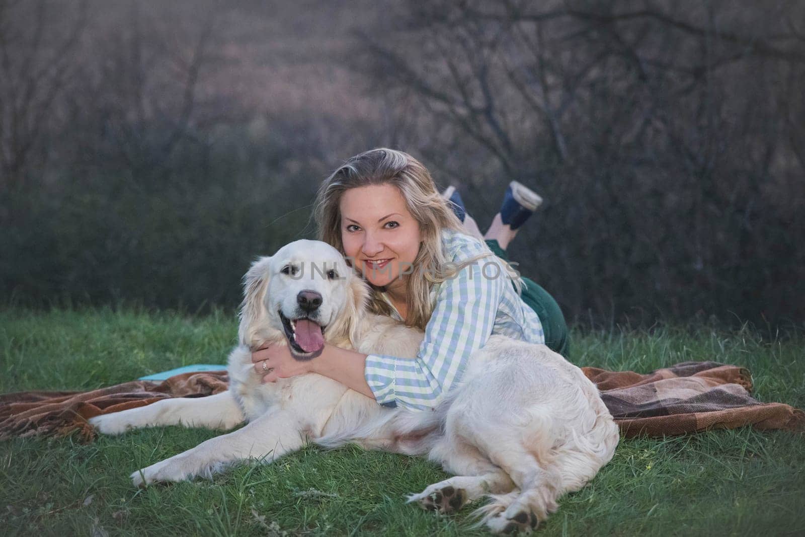 attractive blonde hugging with dog on a plaid in the evening forest