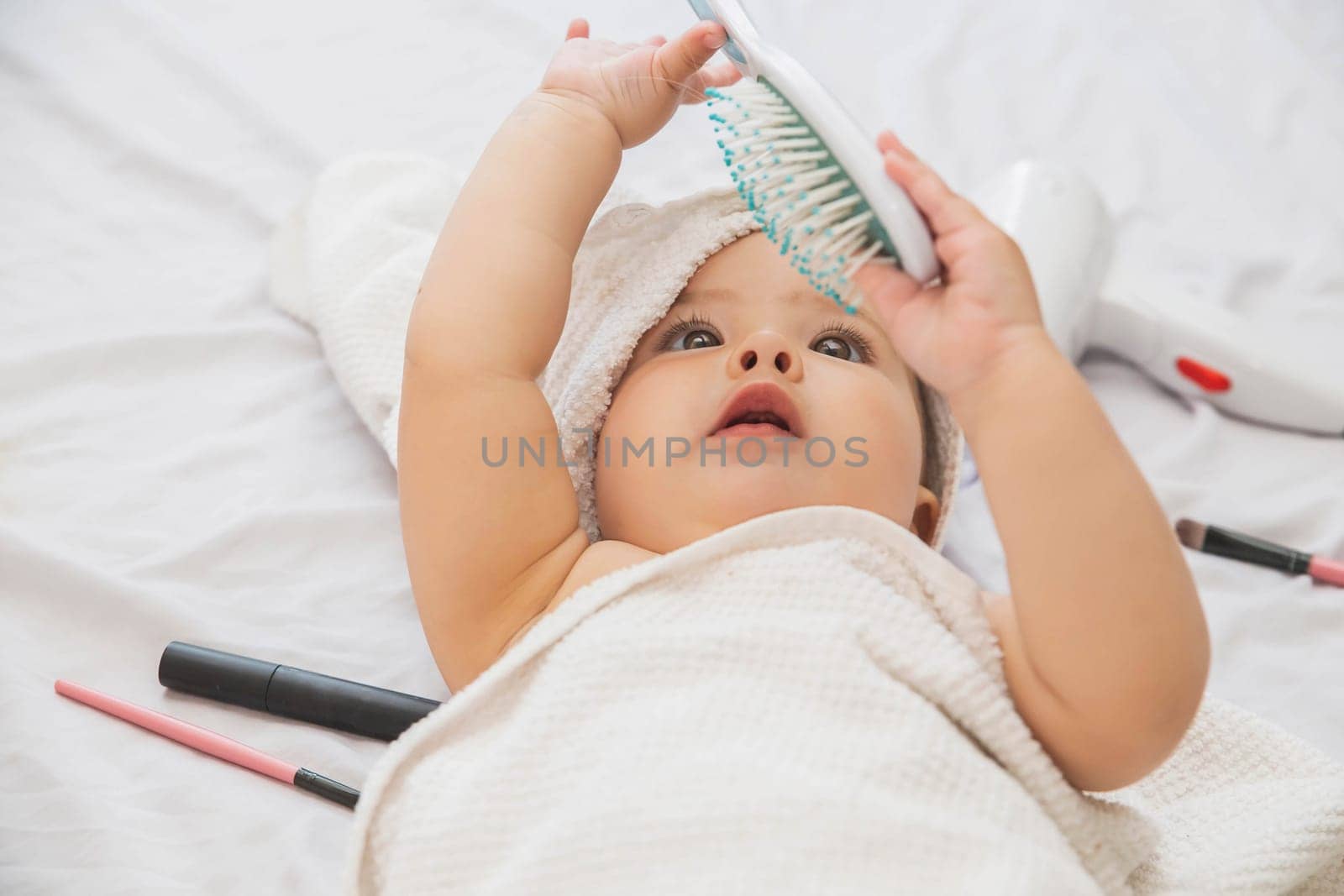 beautiful baby with a white towel on her head looking at a comb.