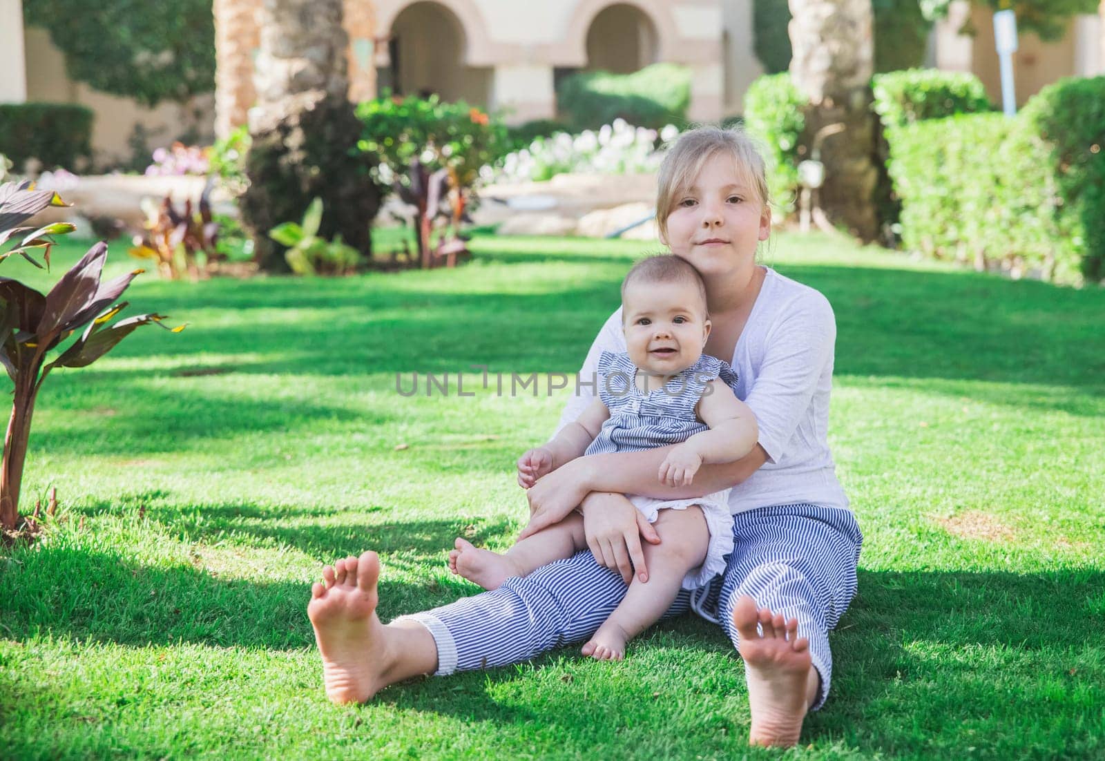 blonde teenager sits with her little sister on the lawn in the yard.