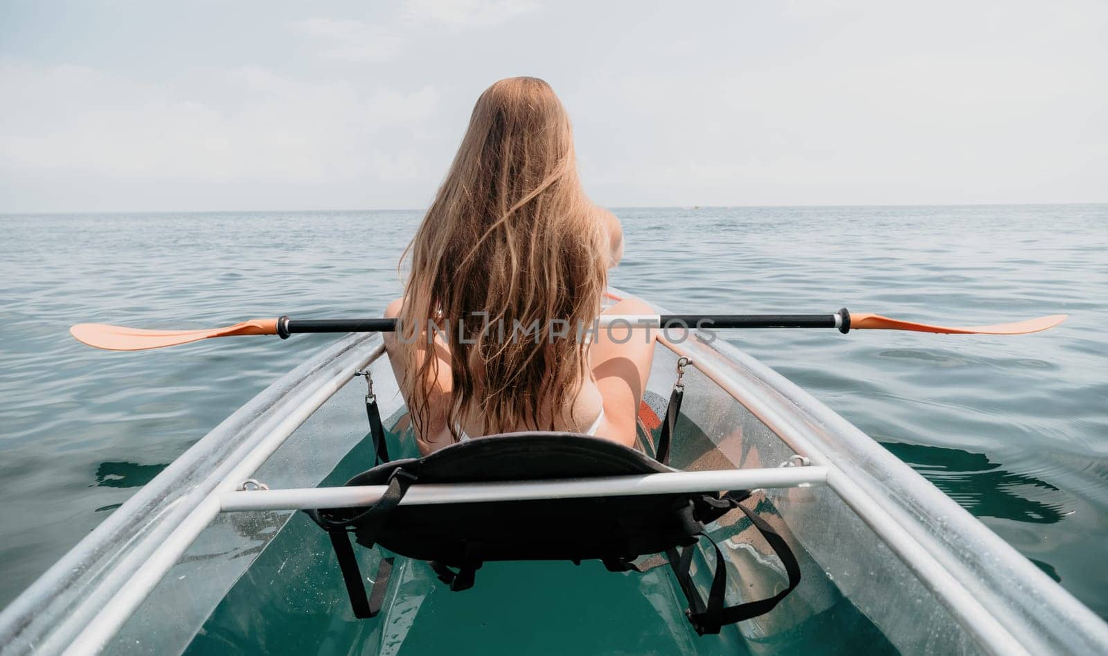 Woman in kayak back view. Happy young woman with long hair floating in transparent kayak on the crystal clear sea. Summer holiday vacation and cheerful female people relaxing having fun on the boat by panophotograph