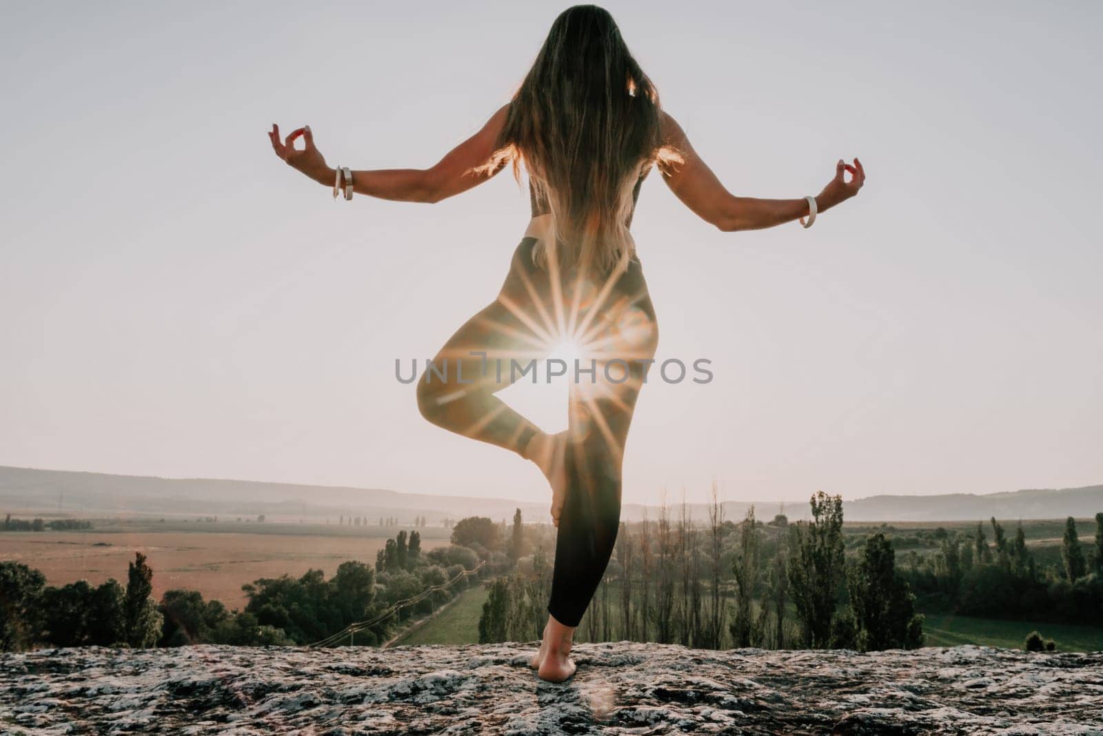 Well looking middle aged woman with long hair, fitness instructor in leggings and tops doing stretching and pilates on the rock near forest. Female fitness yoga routine concept. Healthy lifestyle.