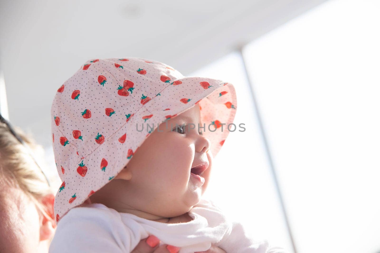 charming newborn girl in hat looks at the sunset and smiles toothlessly