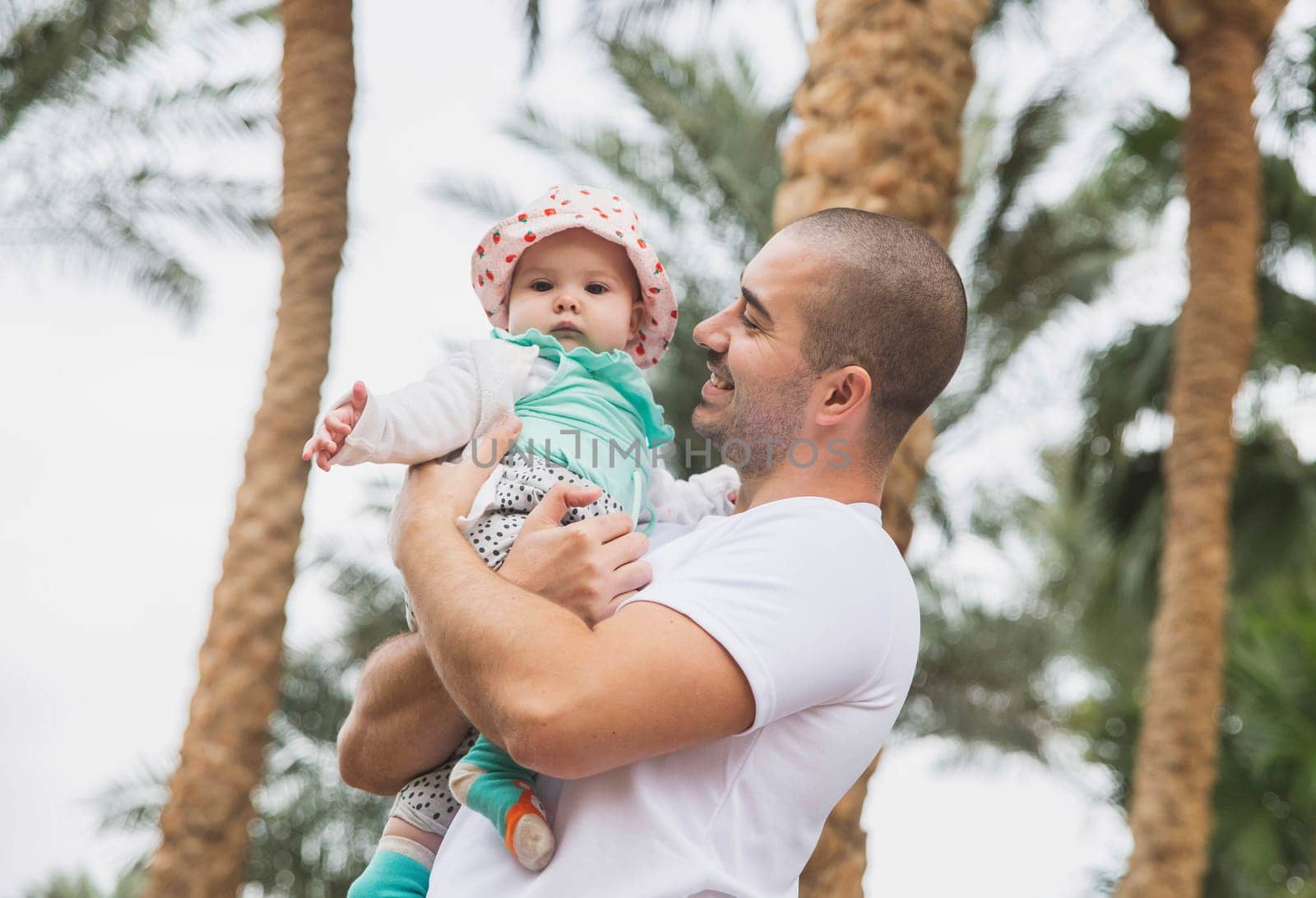 Father holds his charming newborn daughter under the palm trees.