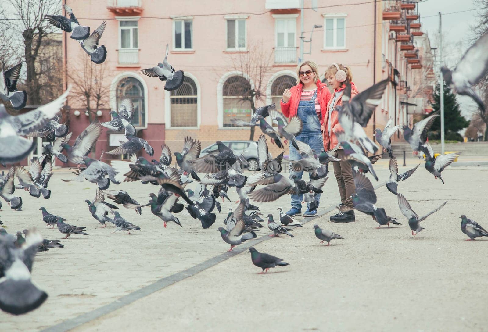 Mom and daughter feed pigeons on the street.