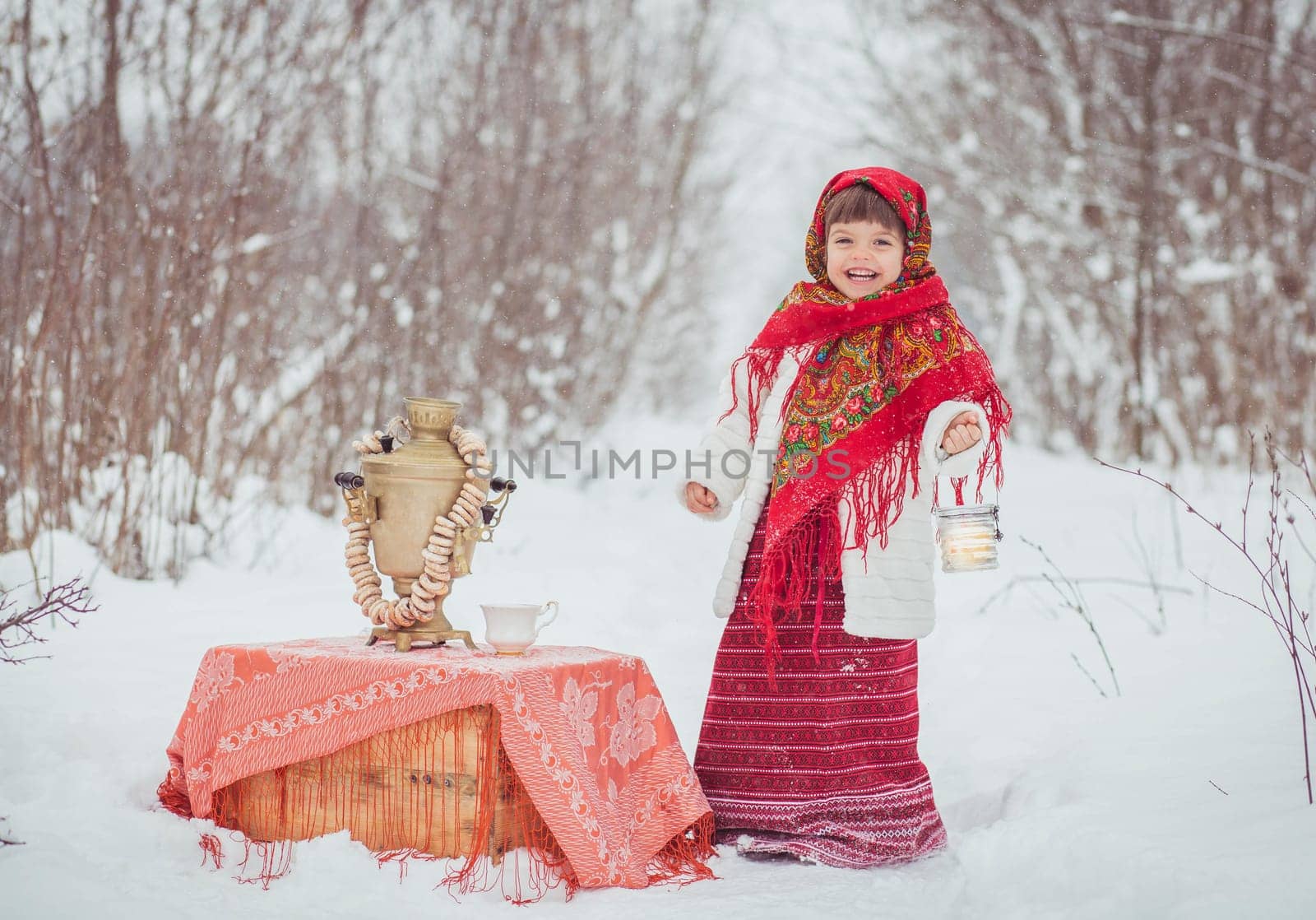 Adorable little girl in old clothes in a winter forest with a samovar and bagels