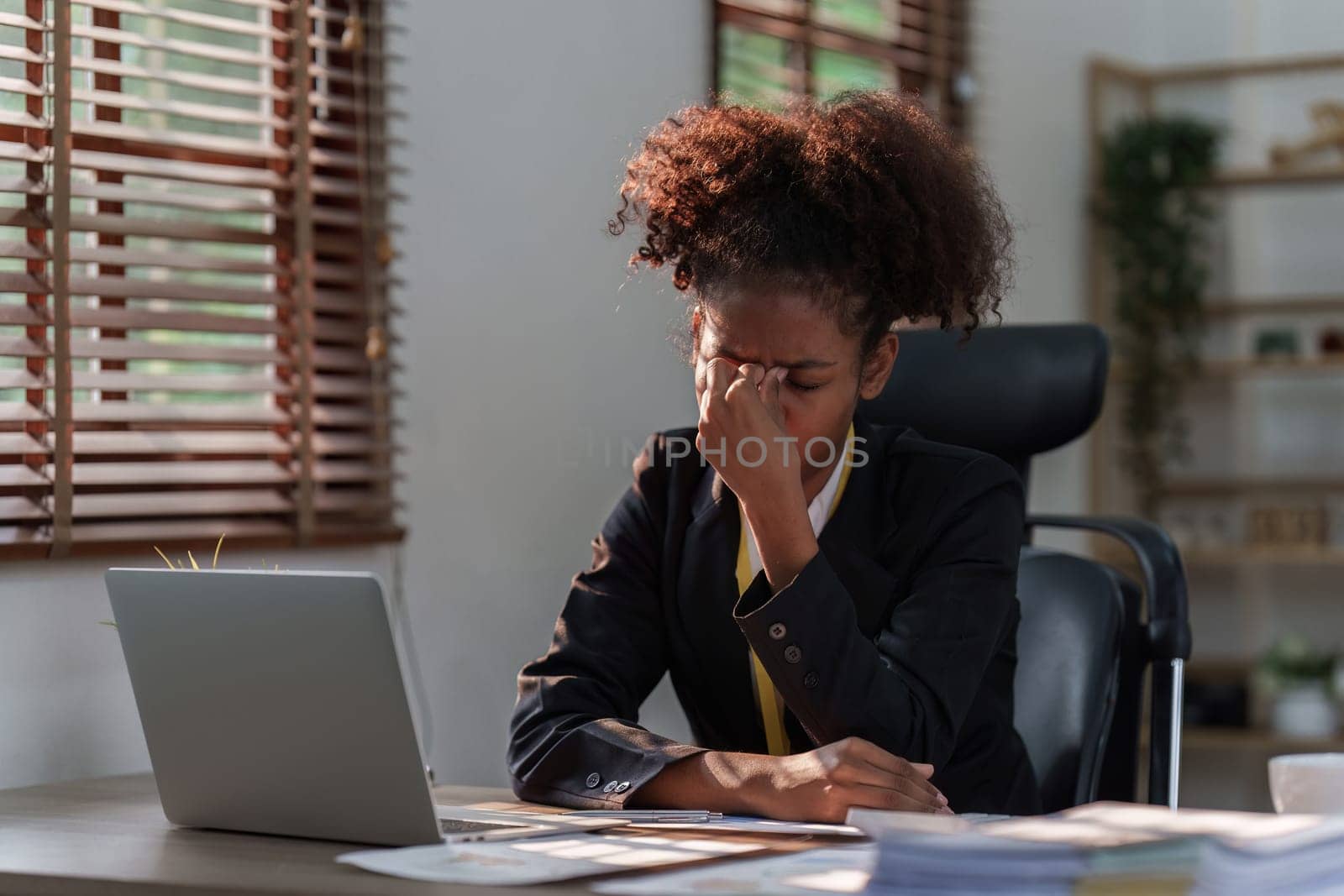 Tired American African business woman in stress works with many paperwork document. migraine attack. Freelance, work from home.