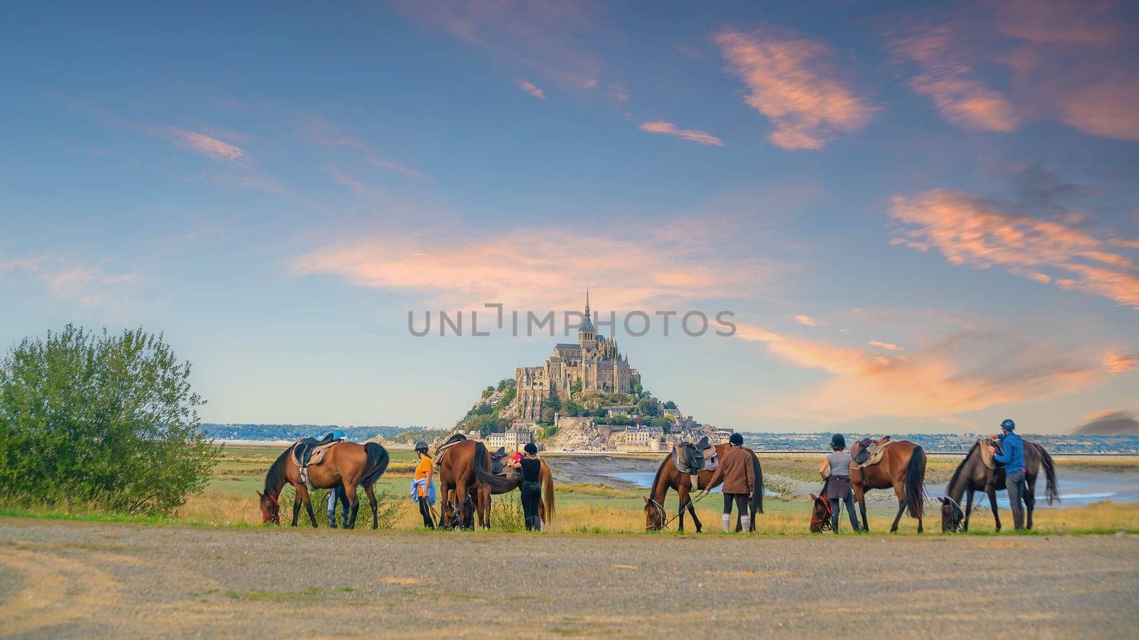 Horses and tourists with famous Le Mont Saint-Michel in Normandy, northern France  at sunset 