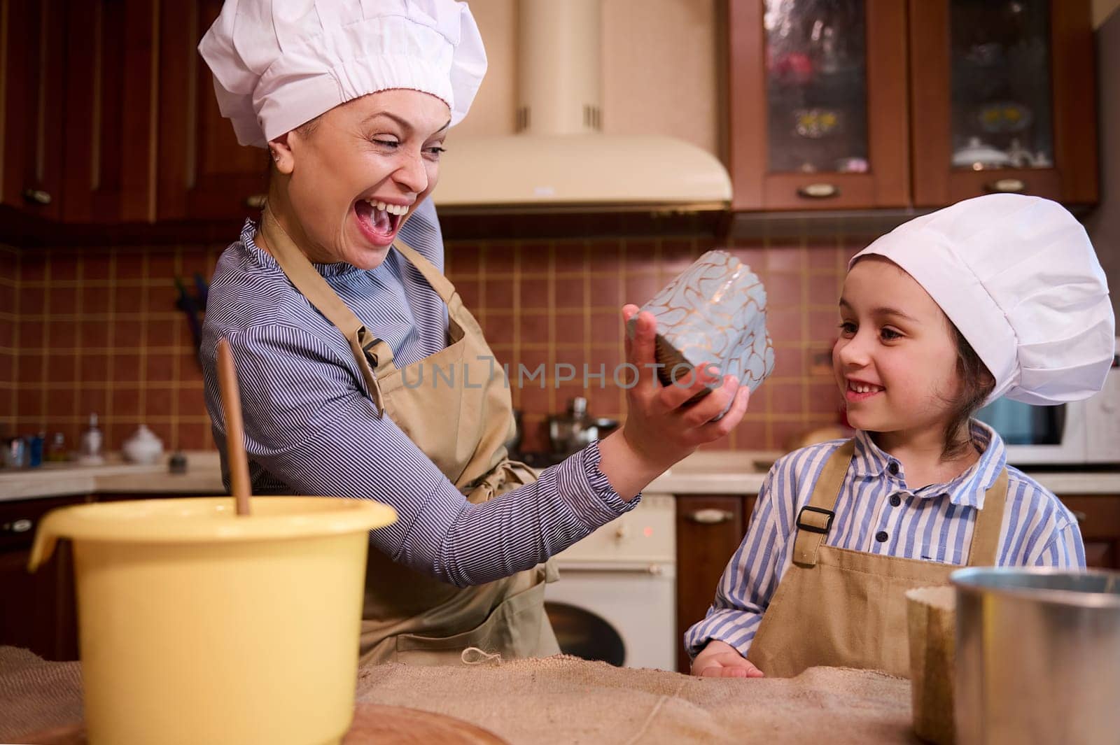 Happy cheerful family, loving mother and cute little daughter have fun together, enjoying festive atmosphere in kitchen while cooking Easter cake, pastries and panettone. People. Lifestyles. Leisures