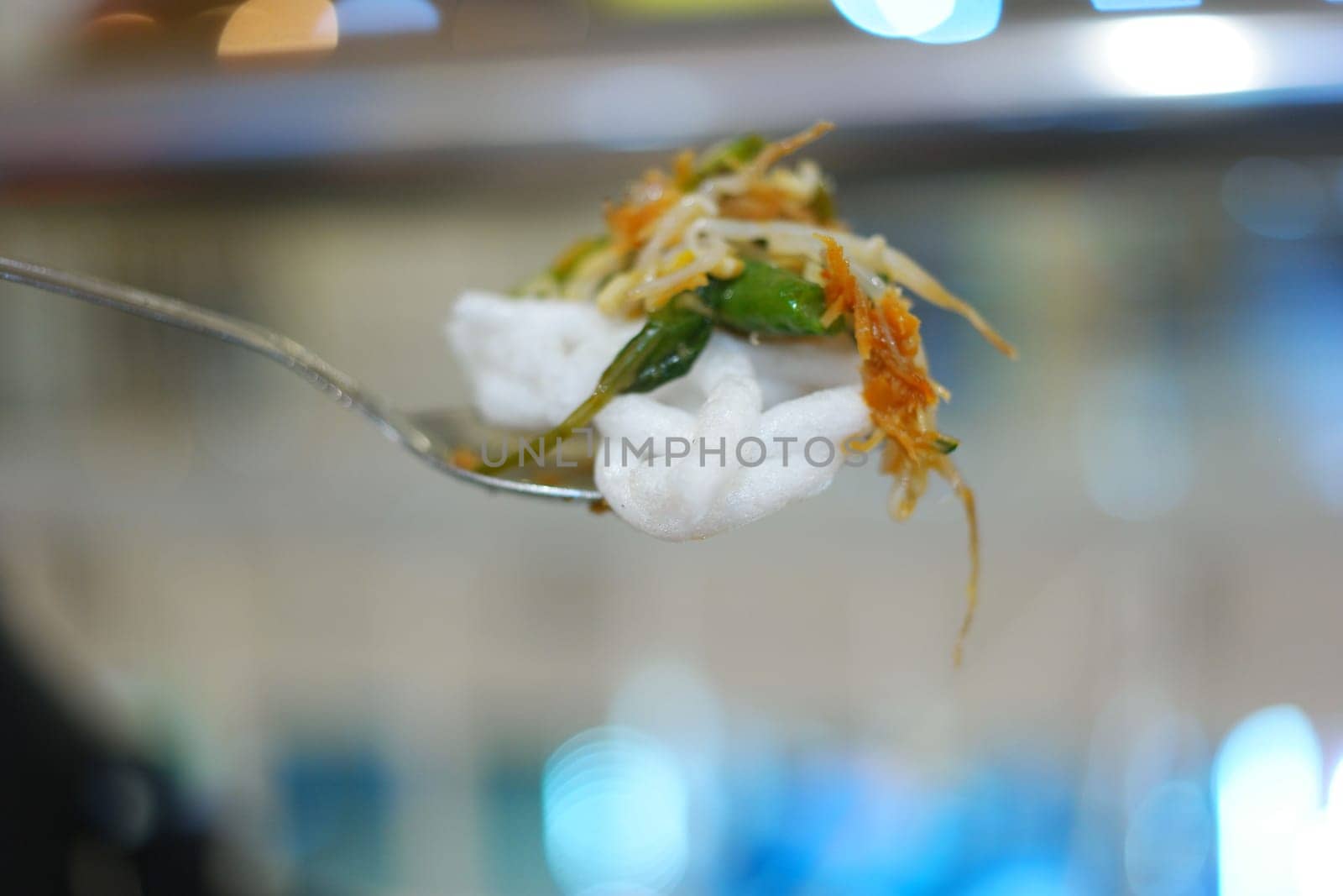 Close-up of a small metal spoon full of rice and vegetables. Bokeh background.