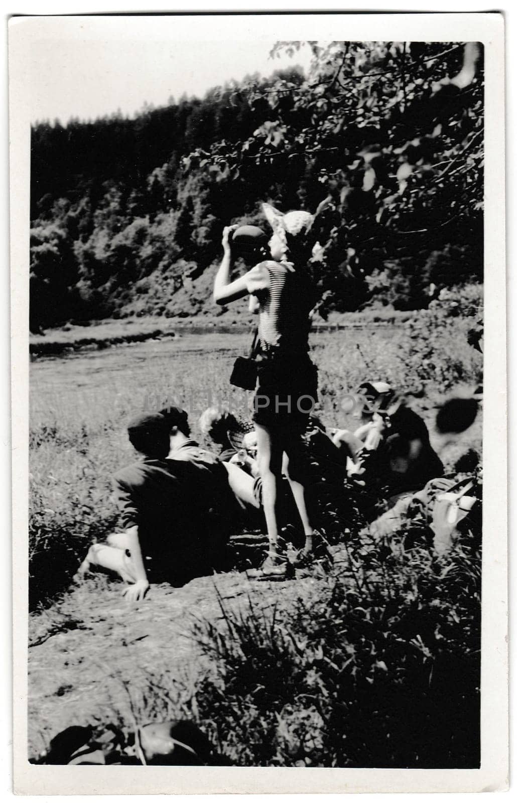 Retro photo shows tourists outside. The boy drinks water from water-flask. Vintage black and white photography. by roman_nerud