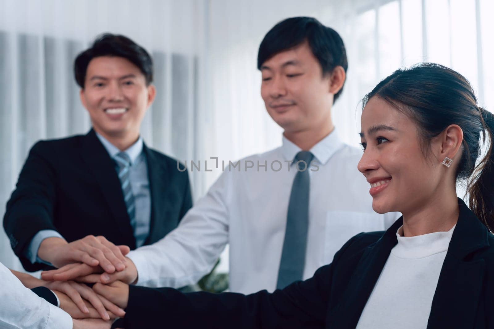 Closeup business team of suit-clad businessmen and women join hand stack together and form circle. Colleague collaborate and work together to promote harmony and teamwork concept in office workplace.