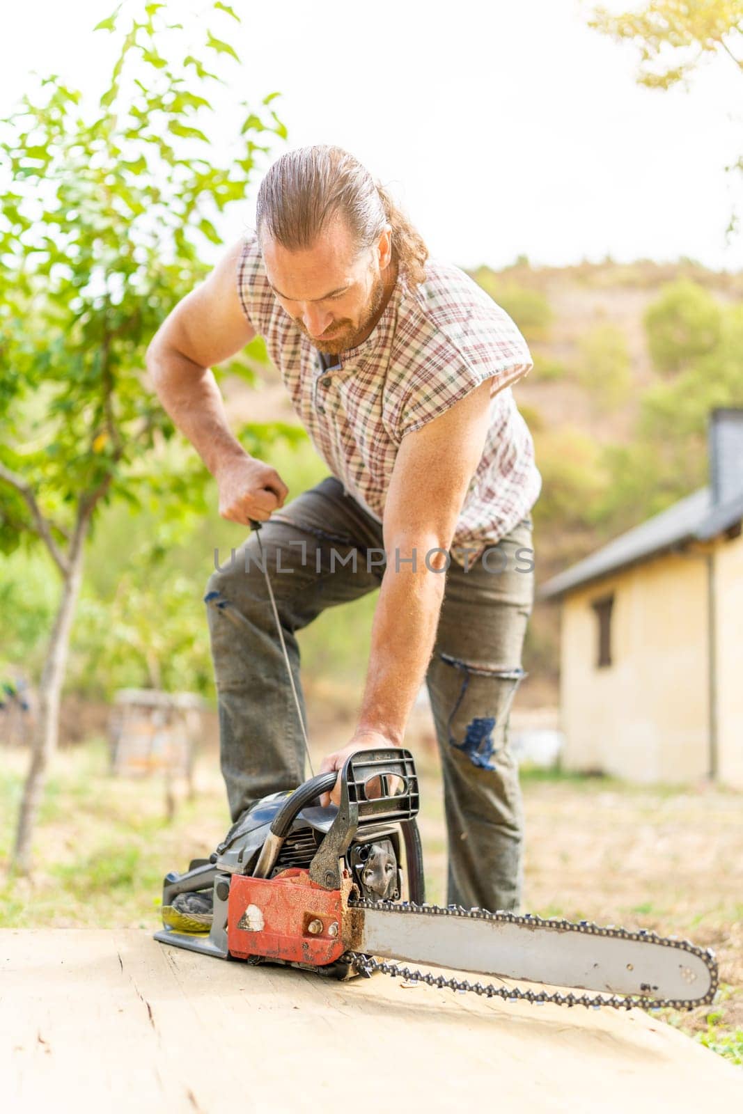 Vertical photo of a woodcutter male ripping up a chainsaw in a garden