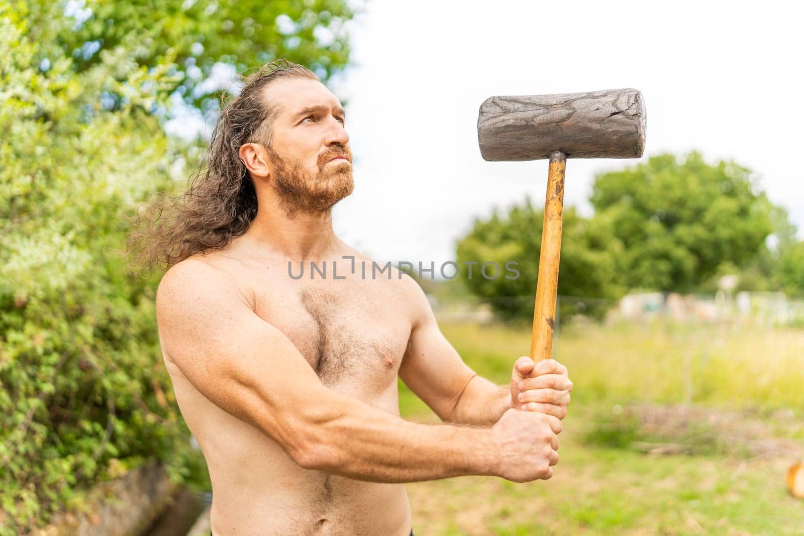 Portrait of a strong wild man with a hammer looking up while standing on a field