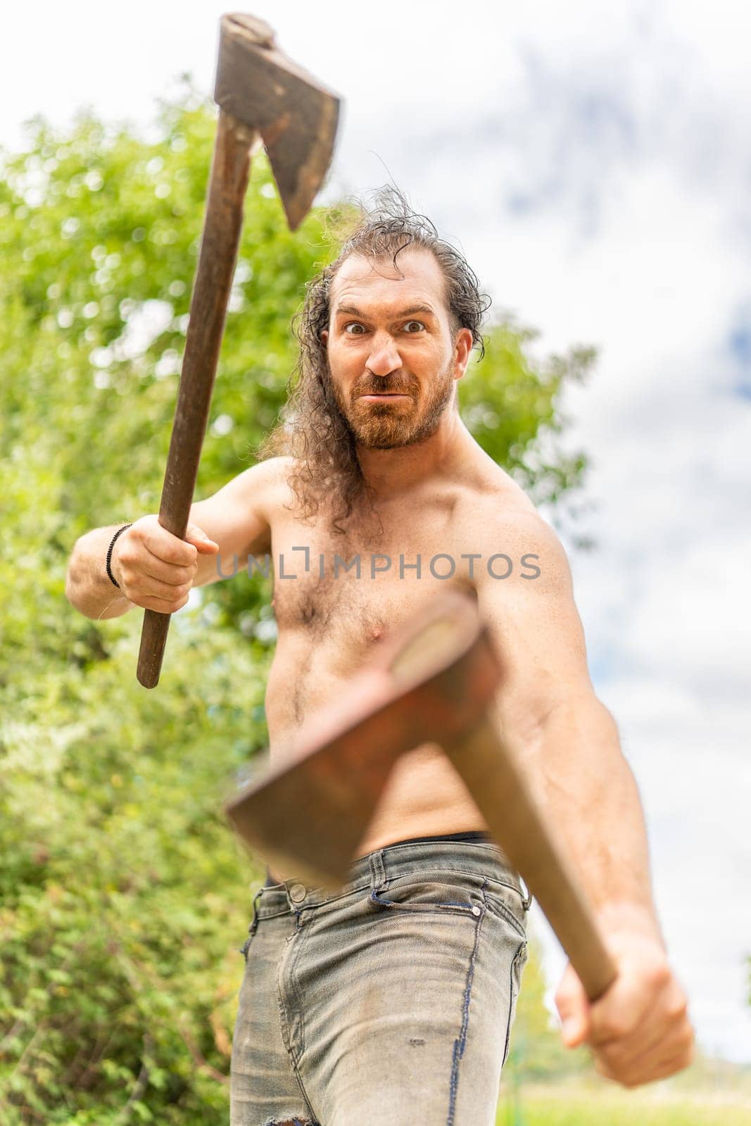 Portrait of Wild man looking at camera while holding two axes