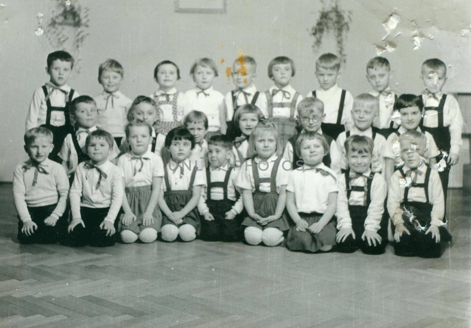 Retro photo shows pupils in the classroom. They pose for a group photography. Vintage black and white photography. Original image is damaged. by roman_nerud