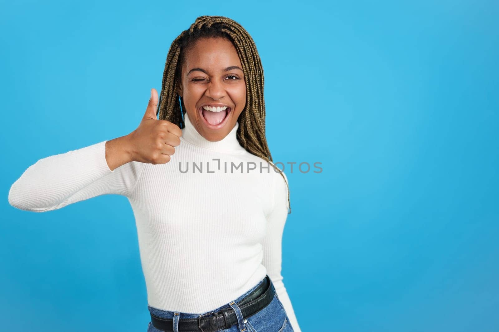 African woman winking as gesturing positively with the thumb up by ivanmoreno