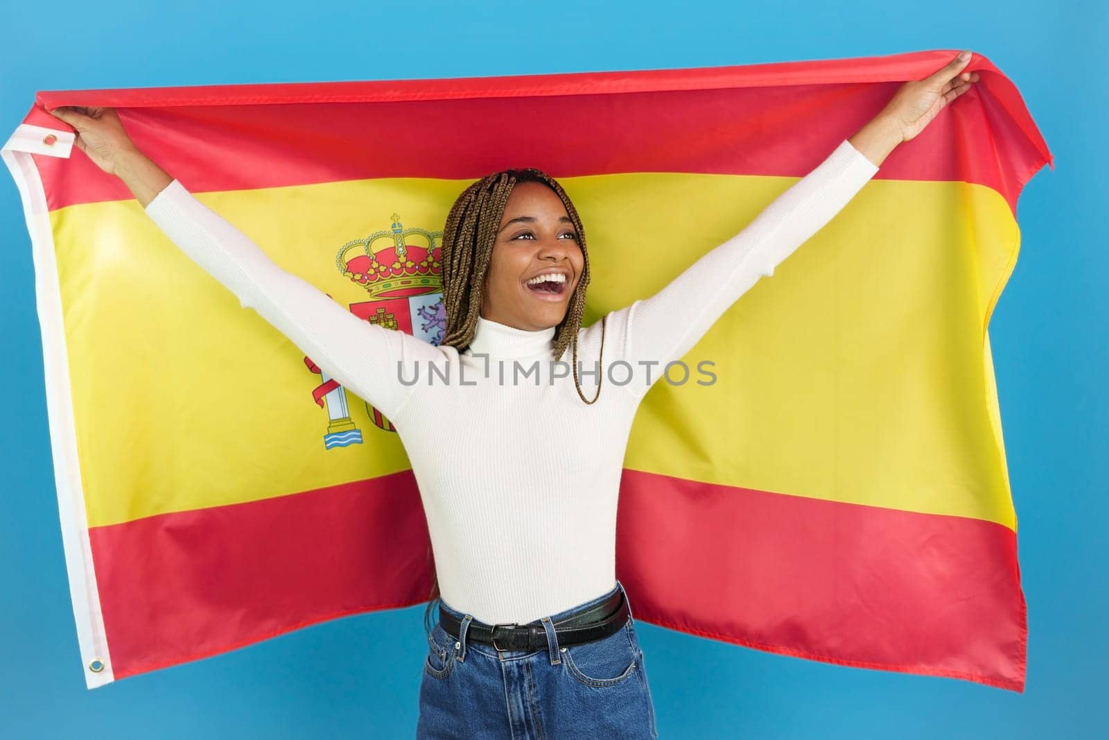 Studio portrait with blue background of a smiling african woman waving a spanish national flag