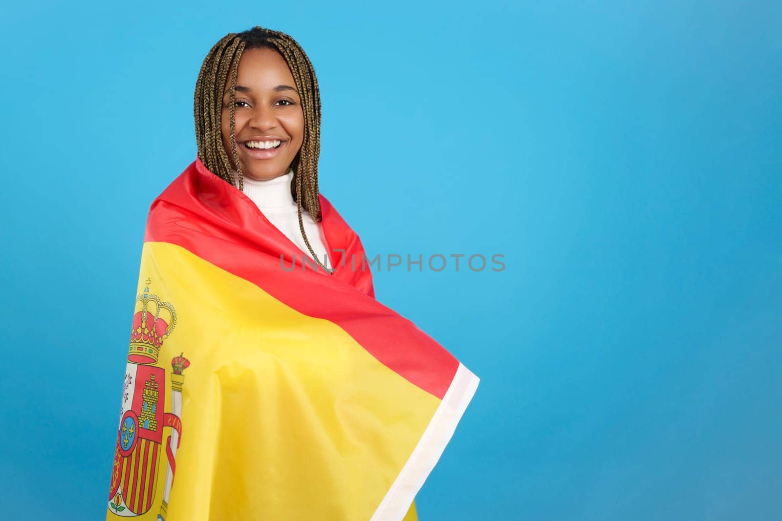 Studio portrait with blue background of an african woman wrapped in a spanish national flag