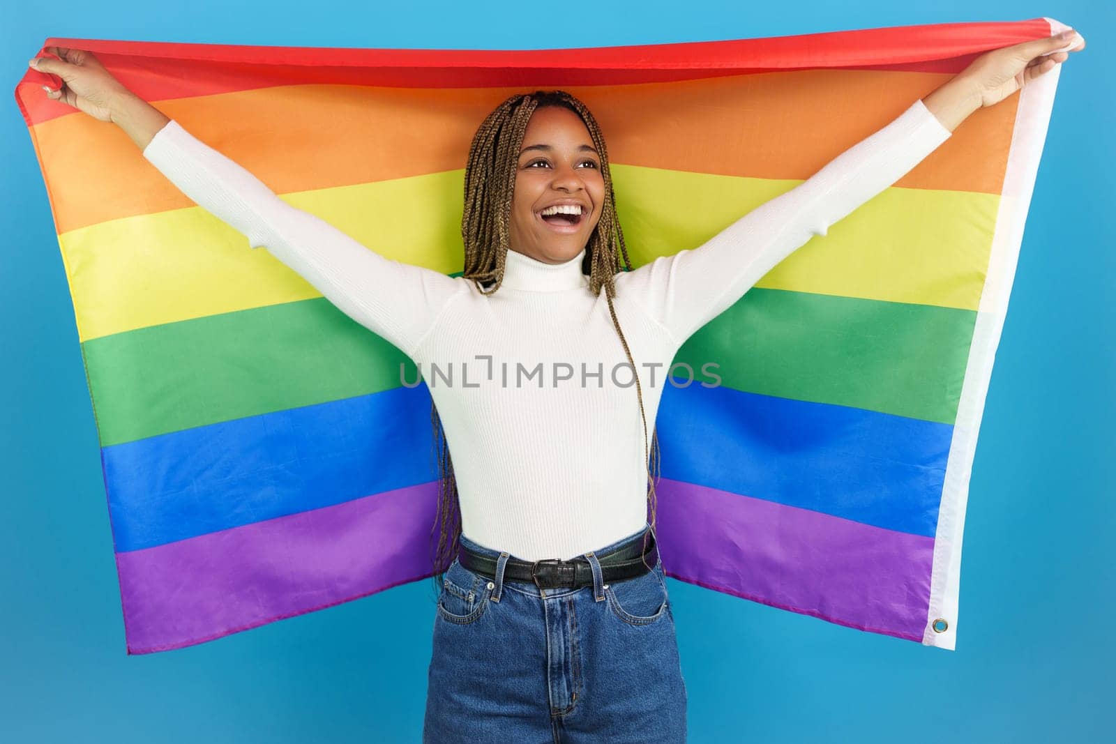 Studio portrait with blue background of an happy african woman raising a rainbow lgbt flag