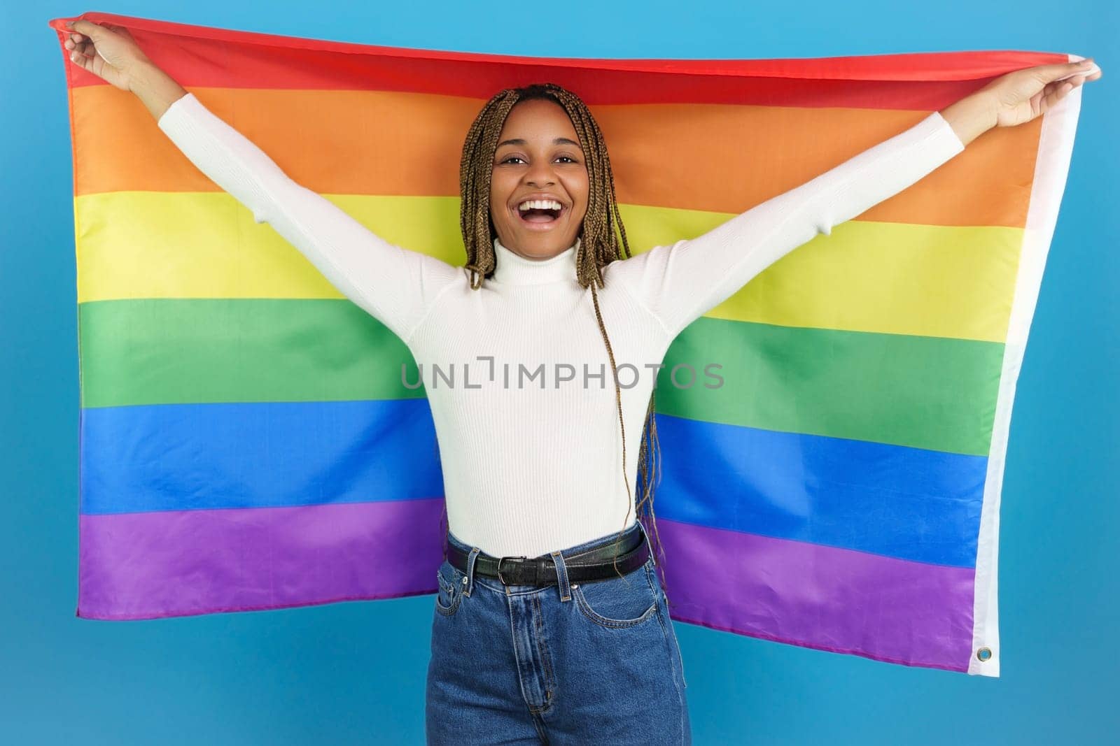Studio portrait with blue background of an smiling african woman waving a rainbow lgbt flag