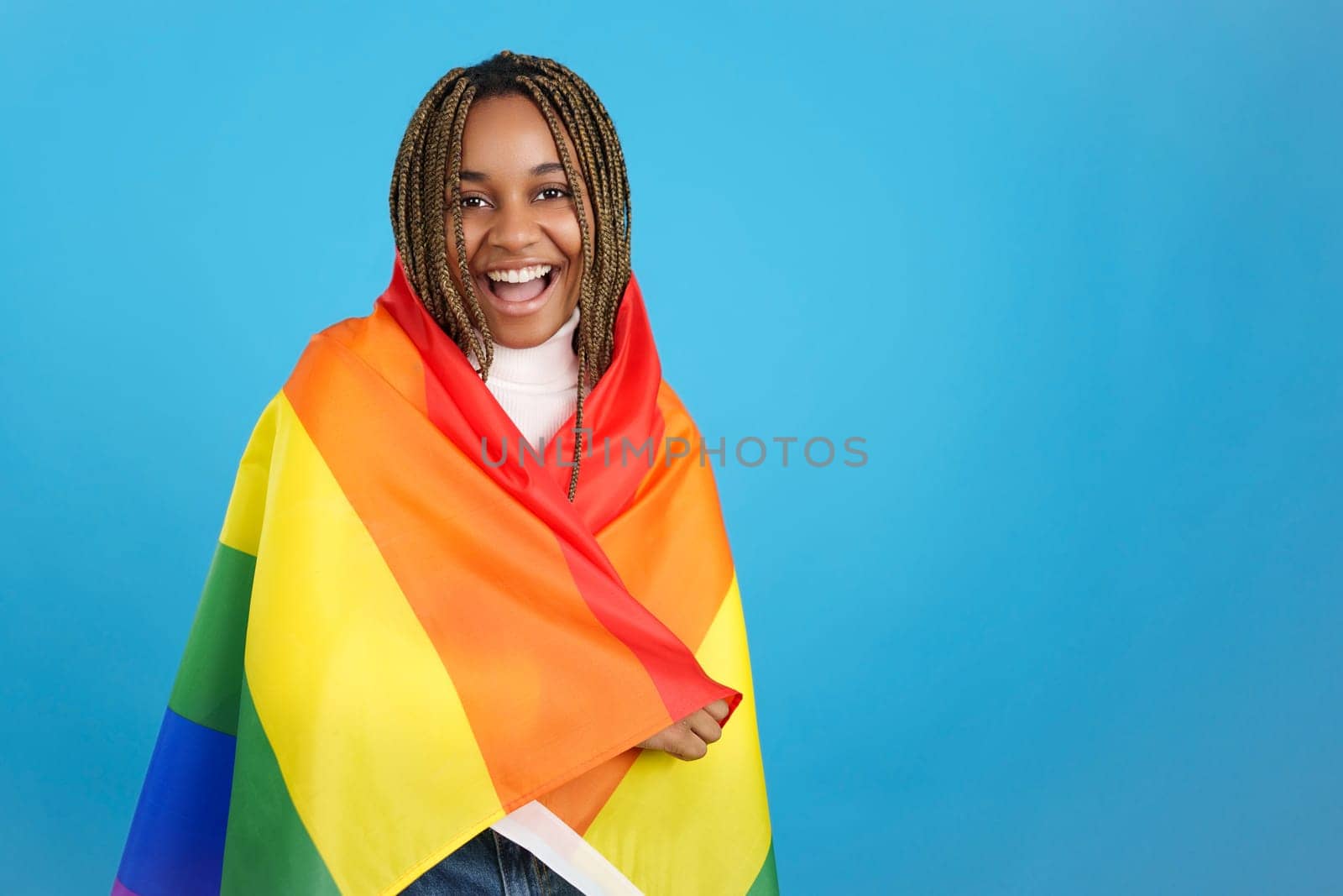 Studio portrait with blue background of a proud african woman wrapped in a lgbt rainbow flag