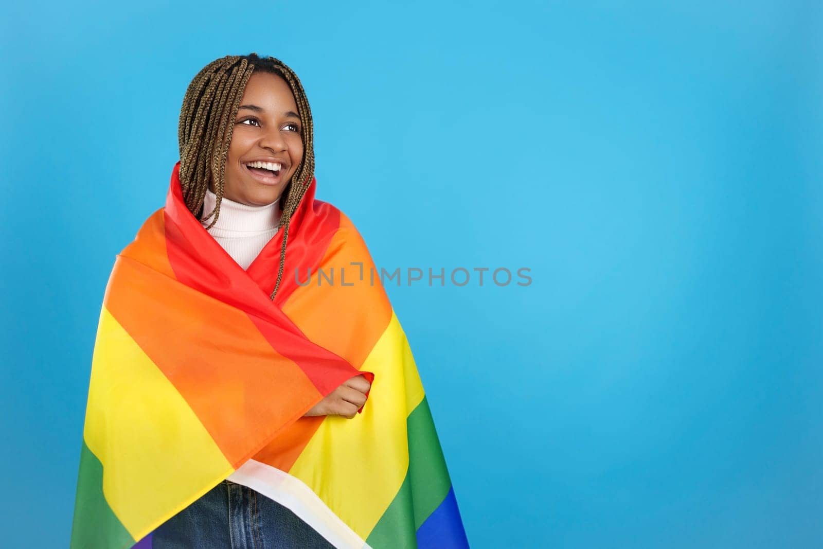 Studio portrait with blue background of a happy african woman wrapped in a lgbt rainbow flag