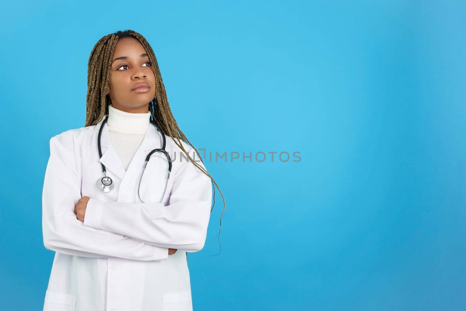 Studio portrait with blue background of a serious African female doctor in uniform with her arms folded