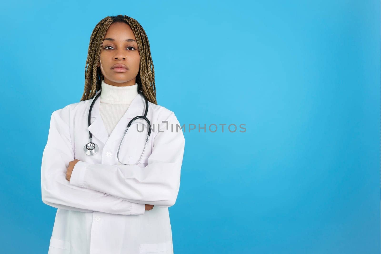 Studio portrait with blue background of a serious african female doctor with arms crossed looking at camera
