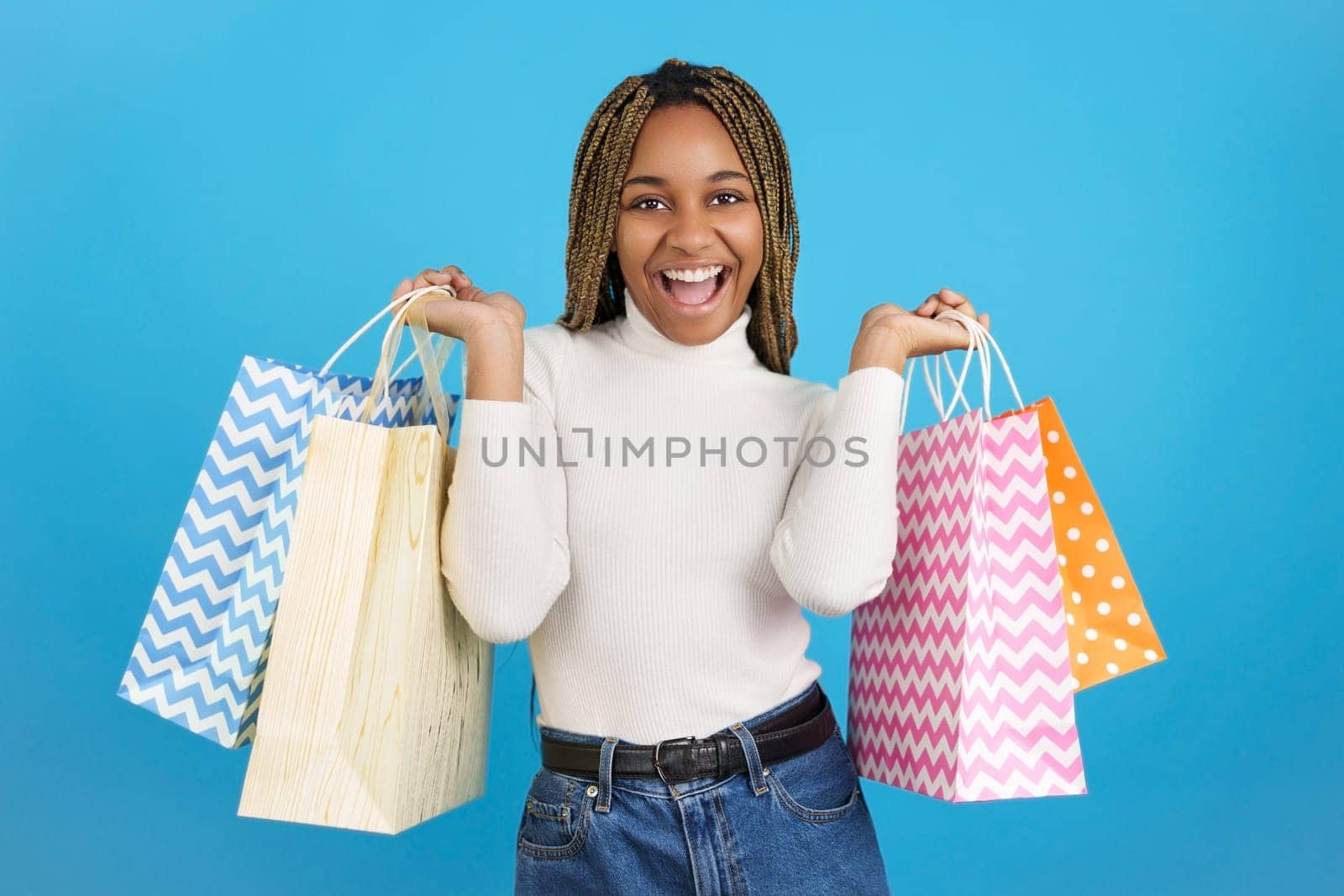 Studio portrait with blue background of a smiling african woman happily carrying shopping bags