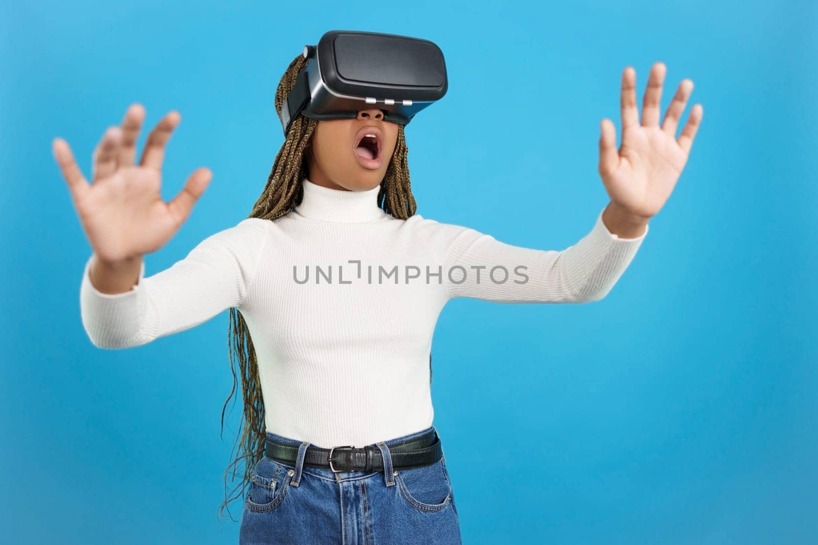 Studio portrait with blue background of a shocked african woman wearing virtual reality goggles