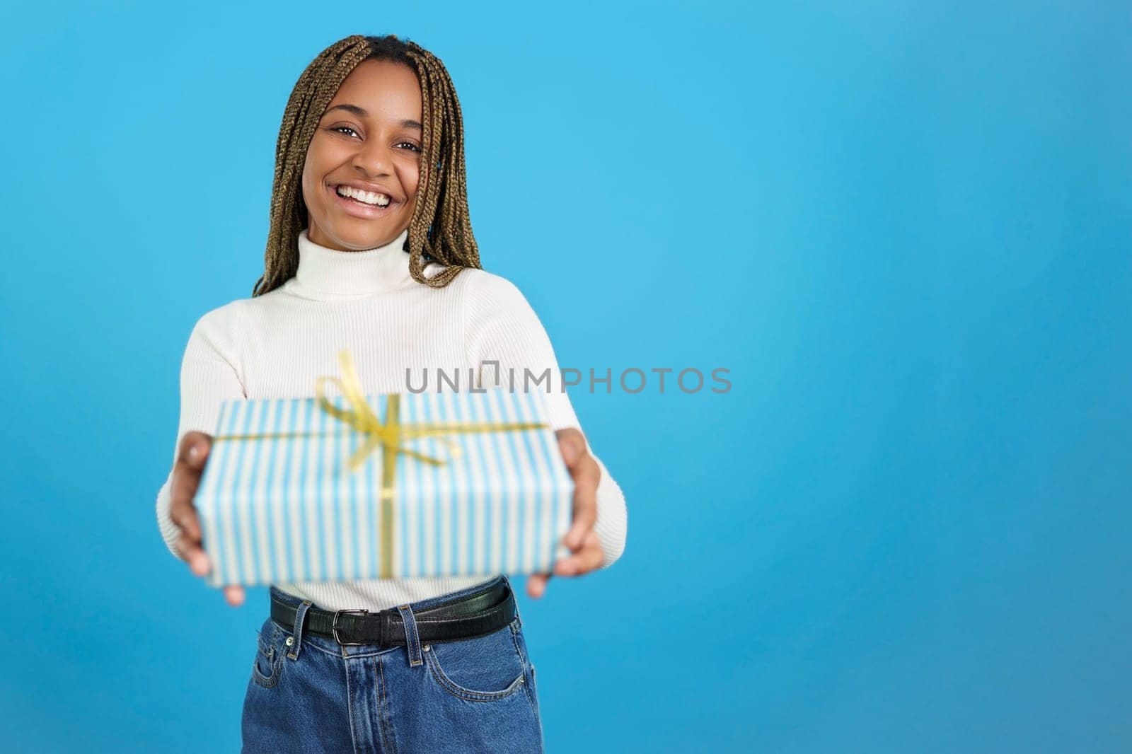 Studio portrait with blue background of an african woman smiling at the camera while giving a gift