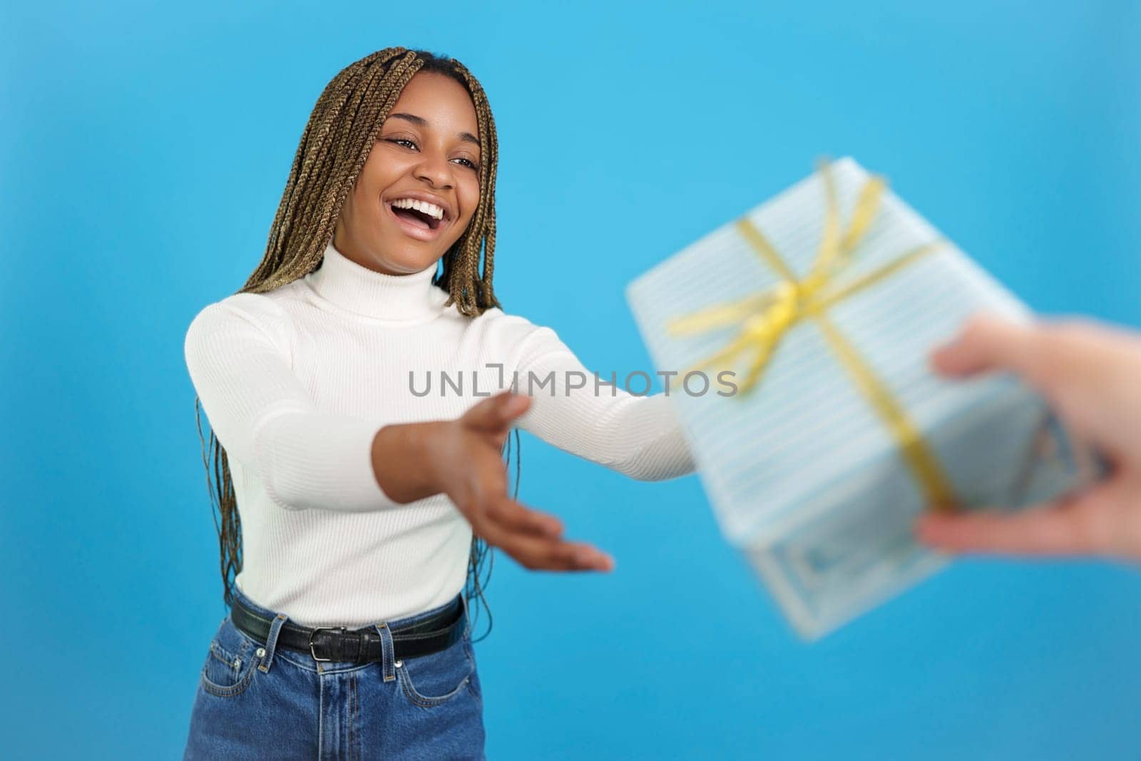 Studio portrait with blue background of an happy casual african woman receiving a gift