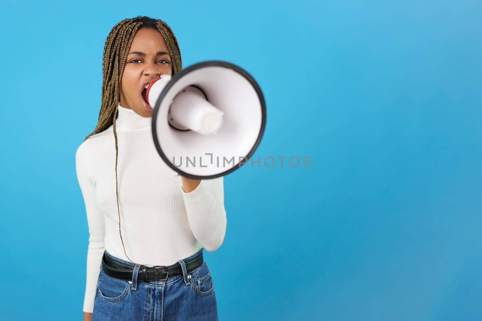 Studio portrait with blue background of an angry african woman protesting while using a loudspeaker