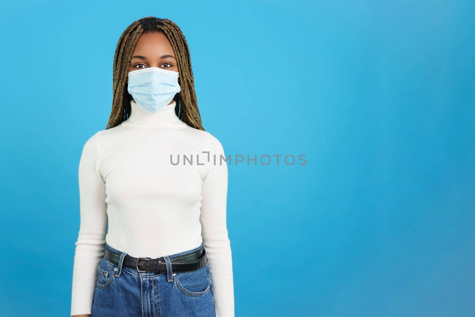 Studio portrait with blue background of an african woman looking at camera while using a protective face mask