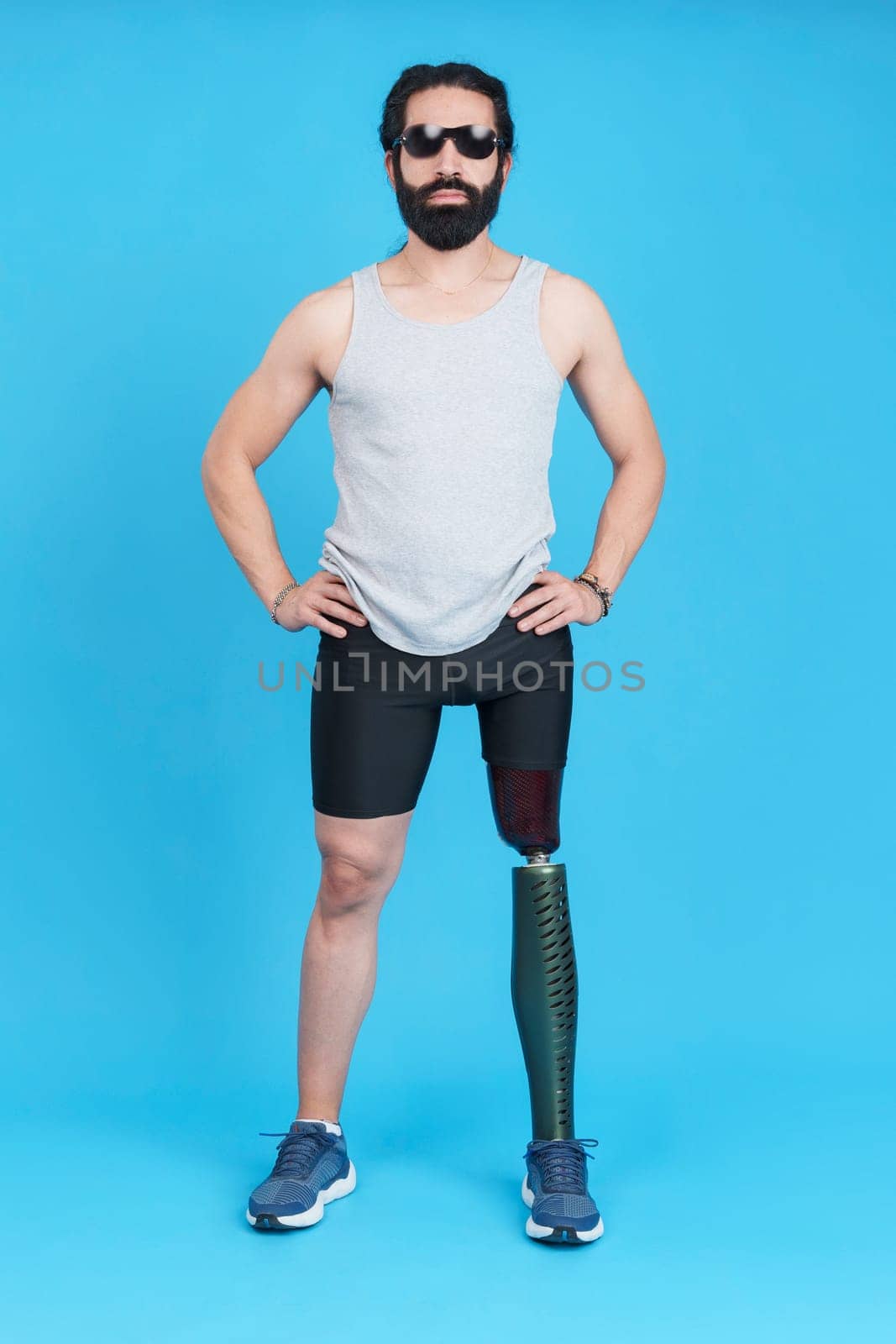 Vertical Studio portrait with blue background of a sportive stylish man with sunglasses standing with a prosthetic leg