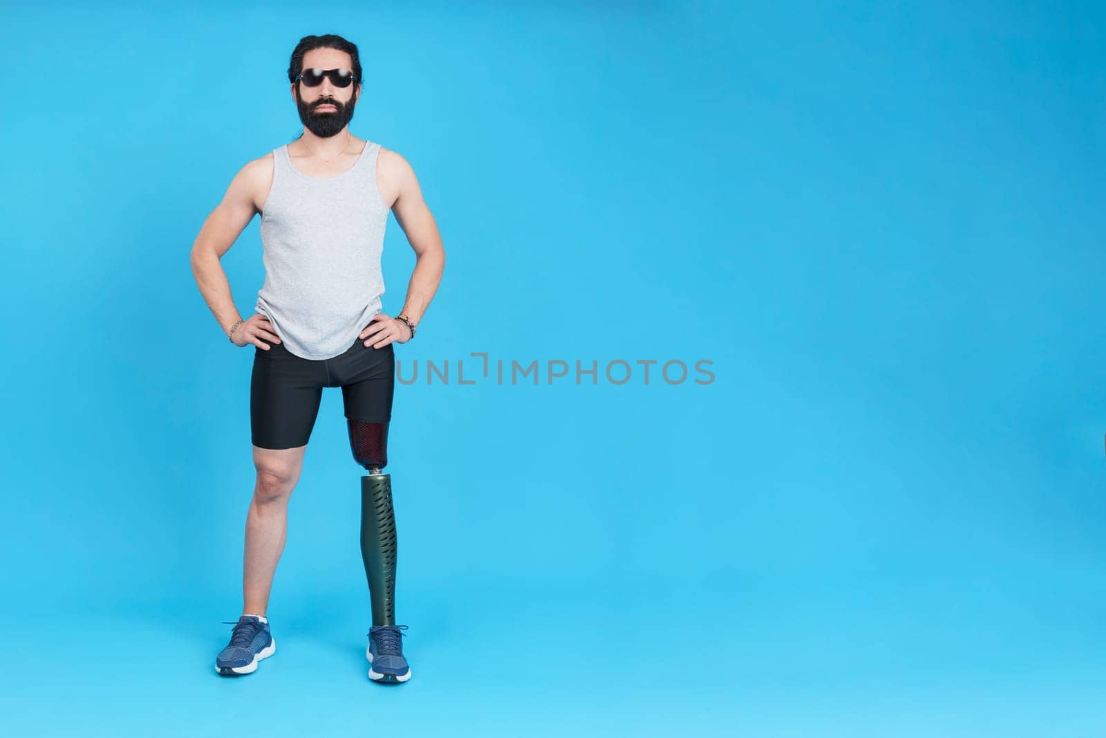 Studio portrait with blue background of a bearded man with sunglasses and a prosthetic leg