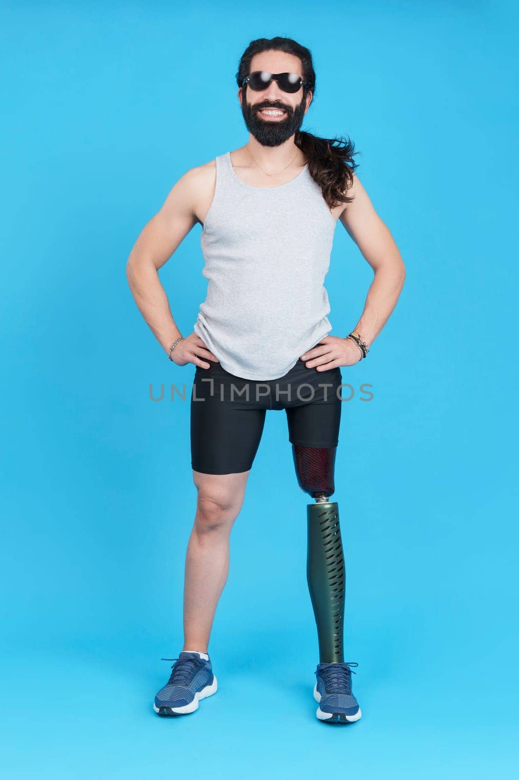 Vertical Studio portrait with blue background of a smiley man with sunglasses standing with a prosthetic leg