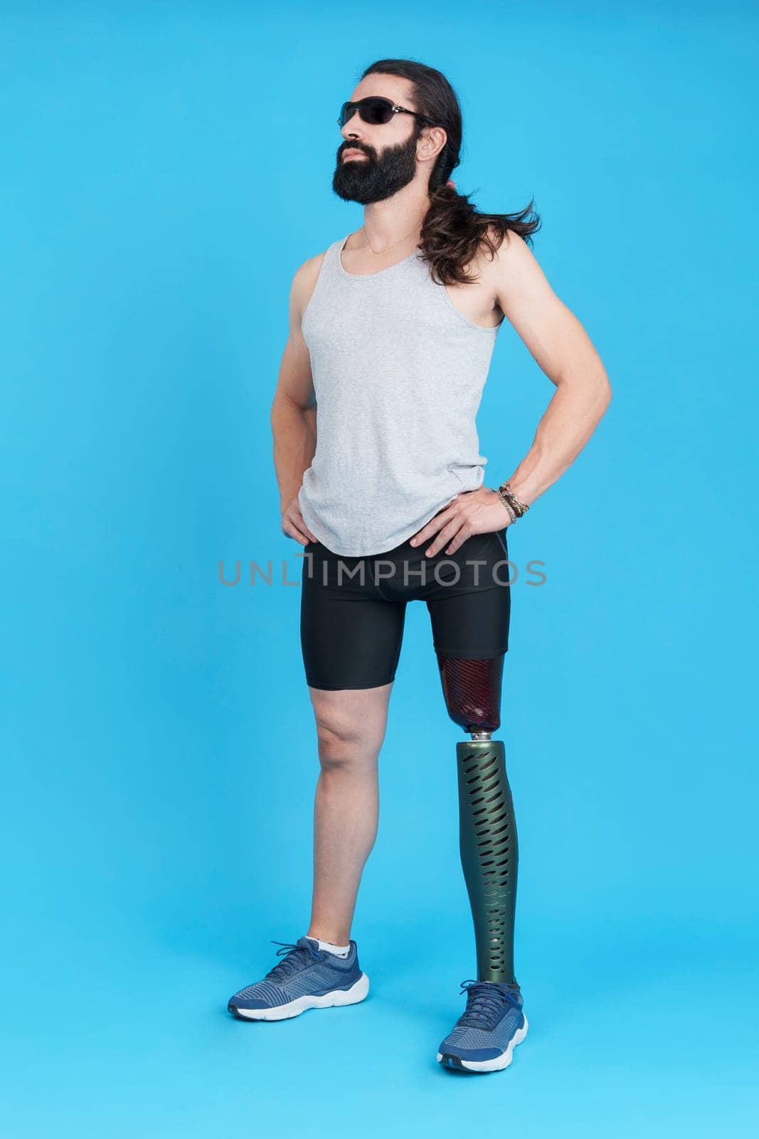 Vertical studio portrait with blue background of a cool man with sunglasses and a prosthesis in the leg