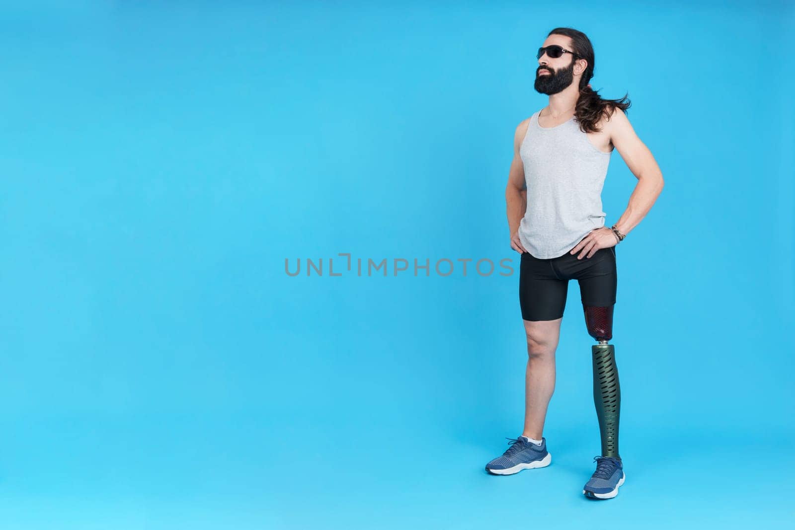 Studio photo with copy space and blue background of a sportive man with sunglasses standing with a prosthetic leg