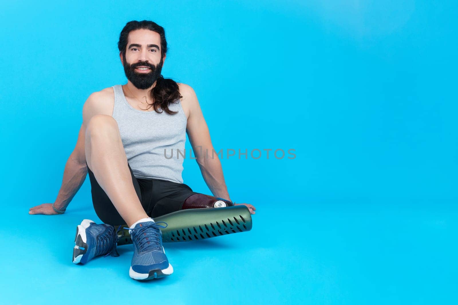 Studio photo with copy space and blue background of a relaxed sportive man with a leg prosthesis sitting on the floor